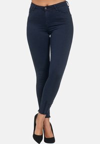 Jeans ajustados de color azul oscuro con una textura suave, diseño de cinco bolsillos y detalles deshilachados en los bajos, combinados con tacones altos negros.