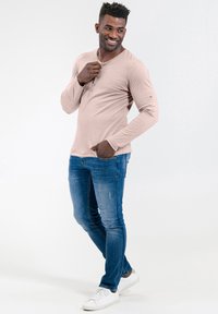 Helles rosa Langarmhemd mit Knopfleiste, kombiniert mit enganliegenden blauen Jeans und weißen Sneakern. Glatte Textur, lässiges Design.