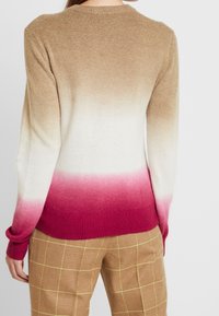 Stickad tröja med en gradientdesign som övergår från ljusbeige till djup rosa vid nederkanten, med ribbade ärmavslut och rund halsringning.