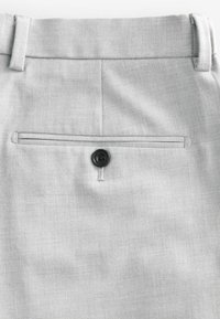 Pantalones gris claro con una tela texturizada, que presentan un bolsillo trasero asegurado con un botón negro y un diseño limpio y de corte recto.