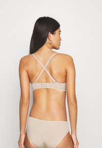 Beige bikini set featuring a crisscross back design and adjustable straps. Soft fabric with minimal hardware and smooth texture.