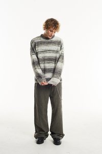 Juostuota megztinis pilkos ir juodos spalvos, derinamas su laisvo kirpimo tamsiomis kelnėmis ir juodais batais su grandinėlės detale ant kelnių.