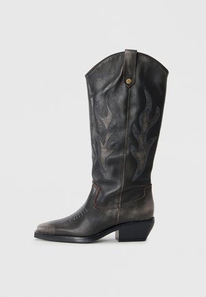 Black leather cowboy boot with flame-like stitching, pointed toe, and a low block heel. Features a decorative metallic button on the side.