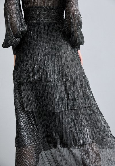 Robe noire à volants présentant une texture plissée, une finition scintillante et de longues manches bouffantes. Le design met en avant un mouvement superposé et une élégance.