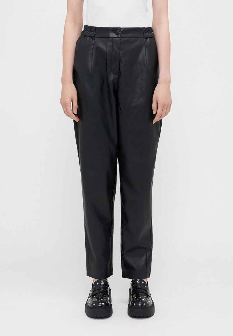 Pantalons en simili cuir noir avec une texture lisse, une taille élastique et une coupe fuselée. Assortis à des chaussures noires épaisses ornées de clous.