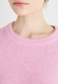 Light pink knit sweater with a ribbed round neckline. Soft texture with subtle variations in shade across the fabric.
