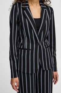 Svart blazer med vertikala vita och ljusblå ränder, enkel knappstängning, slagkrage och två framfickor. Slät tygtextur.