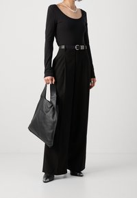 Černý dlouhý rukáv, černé kalhoty s vysokým pasem a plisováním, černá kožená taška a lesklé černé mokasíny. Outfit je monochromatický.