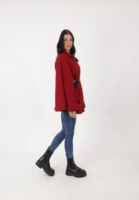 Giacca rossa oversize con colletto, cinched in vita da una cintura nera. Abbinata a jeans skinny blu e stivaletti neri con tacco chunky.