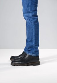 Bottes cheville en cuir noir à finition texturée, dotées d'une semelle robuste. Associées à un jean en denim bleu ajusté.