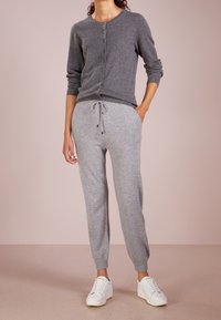 Cardigan en maille grise avec boutons, assorti à un pantalon de jogging gris texturé avec taille à cordon de serrage et poignets côtelés, porté avec des baskets blanches.