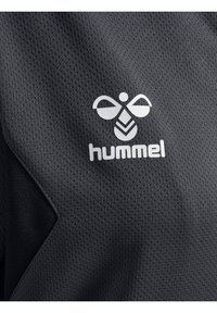 Sort åndbart stof med hvidt stiliseret bi-logo og "hummel" tekst trykt på overfladen.