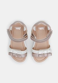 Sandal z bež in belo zasnovo, s sijajno srebrno pentljo, nastavljivim bočnim trakom in teksturiranim podplatom.