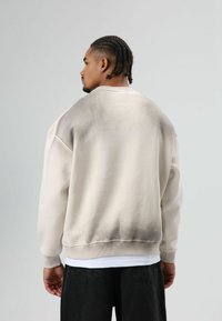 Lichtbeige sweatshirt met een verloop naar een donkerdere tint bij de zoom. Voorzien van een ronde hals, geribbelde manchetten en een losse pasvorm.