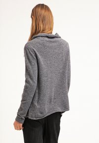 Šedý, měkký svetr s vysokým límcem, uvolněným střihem a dlouhými rukávy. Hladká textura, zakřivený lem a minimální detaily.