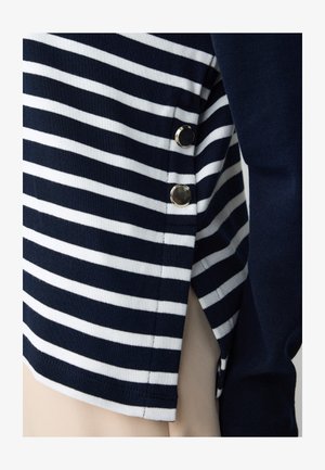 Gestreepte top in marineblauw en wit, van zacht stof, met metalen accenten aan de zijkant en sluitingdetails voor extra stijl.