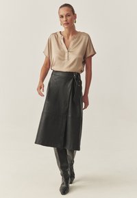 Satinbeige blus med krage och knappar, i kombination med en svart läderfodralkjol med knytning och dekorativa knappar. Svart höga stövlar.