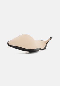 Chausson noir et beige avec un design élégant et incurvé, finition mate lisse et semelle intérieure texturée pour une meilleure adhérence.