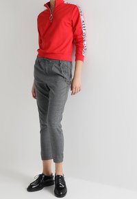 Röd zip-up sweatshirt med vita sidostråk, matchad med grå rutiga, avsmalnande byxor med kedjedetalj. Svarta snörskor fulländar looken.