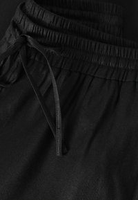Ceinture élastique noire avec cordon sur tissu doux, montrant la texture et les détails de couture.