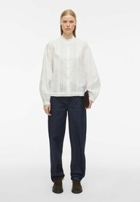 Witte blouse met gerimpelde kraag, puffmouwen en textuurelementen. Gecombineerd met donkerblauwe losse jeans en bruine schoenen.