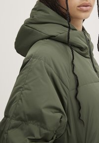 Grüne gepolsterte Jacke mit Kapuze, ausgestattet mit einem Reißverschluss vorne und gestickten Details. Glatte Textur und lässige Passform.