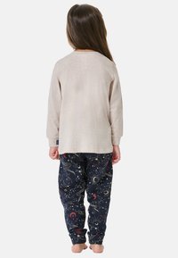 Helle beige Langarmbluse, kombiniert mit marineblauen Hosen, die bunte himmlische Muster aufweisen, eine weiche Textur und elastische Bündchen haben.