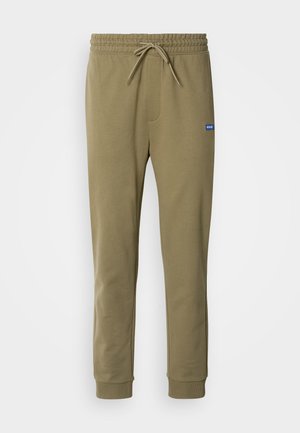Pantaloni della tuta verde oliva con vita elastica e stringi vita. Presentano tasche laterali e polsini a costine. Realizzati in materiale morbido e elastico.