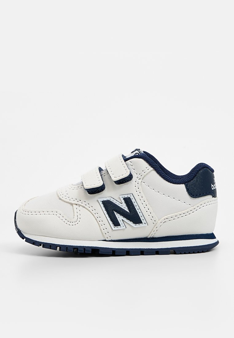 Baskets pour enfants avec une tige synthétique blanche, des accents bleu marine, des straps velcro, des semelles texturées et un grand logo "N" sur le côté.