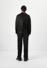 Ensemble noir texturé comprenant une chemise ample et un pantalon. La chemise a un col et un ourlet brut, tandis que le pantalon est légèrement fuselé.