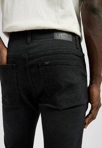 Czarne dżinsy z denimu o dopasowanym kroju, z skórzaną metką na pasku i złotym przeszyciem na tylnej kieszeni.