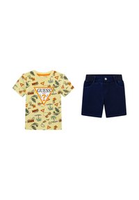 T-shirt di cotone gialla con pattern tropicali e logo "GUESS", abbinata a pantaloni corti in jeans blu scuro con tasche frontali e vita.