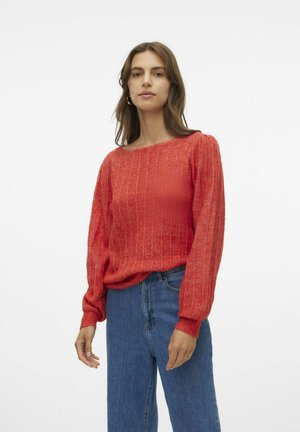 Röd, ribbad stickad tröja med vid halsringning och långa, något puffade ärmar, ihop med blå, högmidjade jeans.