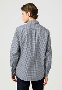 Camicia da uomo a maniche lunghe con un motivo a quadri blu e bianchi, colletto button-down e orlo curvo, realizzata in tessuto di cotone lavorato.