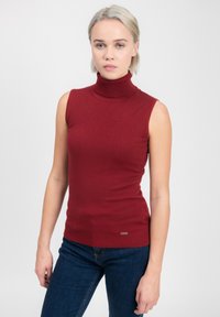 Top senza maniche rosso a collo alto in morbido tessuto knit con texture a costine; presenta una silhouette aderente e un piccolo tag decorativo dorato sull'orlo.