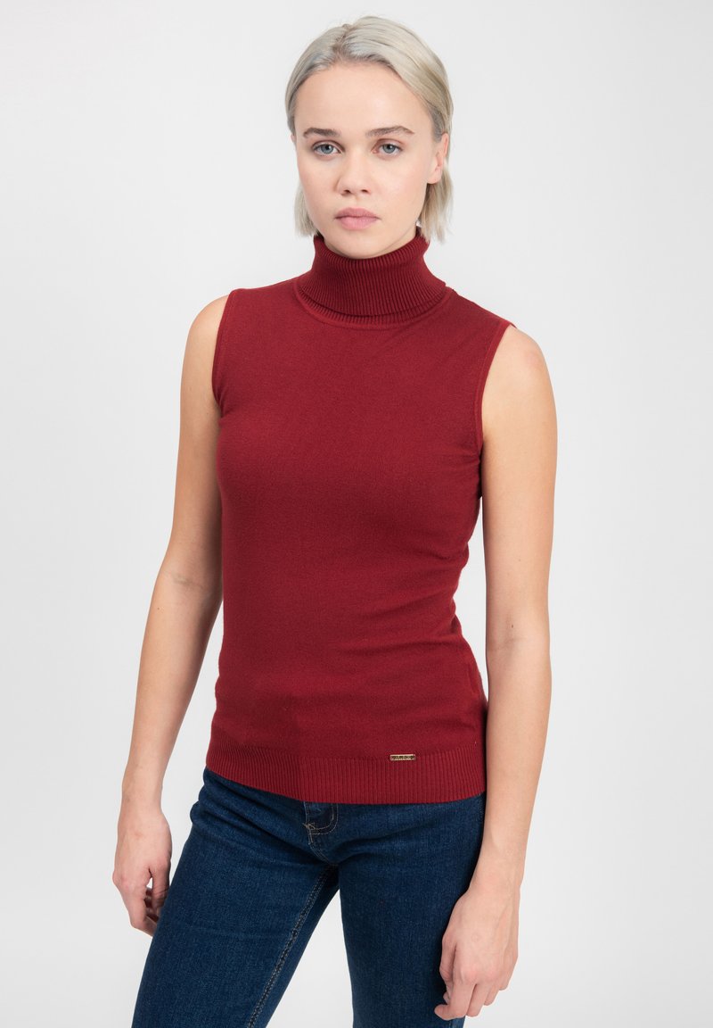 Top senza maniche rosso a collo alto in morbido tessuto knit con texture a costine; presenta una silhouette aderente e un piccolo tag decorativo dorato sull'orlo.