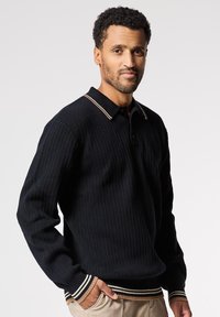Polo a maniche lunghe nero a coste con colletto strutturato, caratterizzato da un accento a righe. Il tessuto sembra spesso e testurizzato, adatto per un abbigliamento informale.