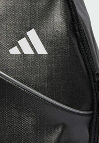Detailní záběr na černou texturovanou tašku s bílým logem Adidas a viditelným zipem na boku.