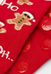 Czerwone skarpetki z wzorem piernikowych ludzików i białymi akcentami, ozdobione błyszczącymi czerwonymi kropkami dla dodatkowej przyczepności. Napis "Ho Ho Ho."