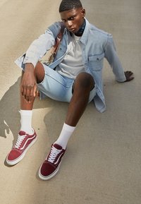 Baskets en daim bordeaux avec des lacets blancs, portées avec des chaussettes blanches. Shorts en jean bleu clair et une veste en jean claire portée sur un t-shirt gris.