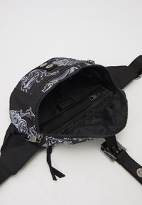 Black fabric bag with white intricate print, featuring a zippered compartment and adjustable strap, showcasing a sleek and functional design.