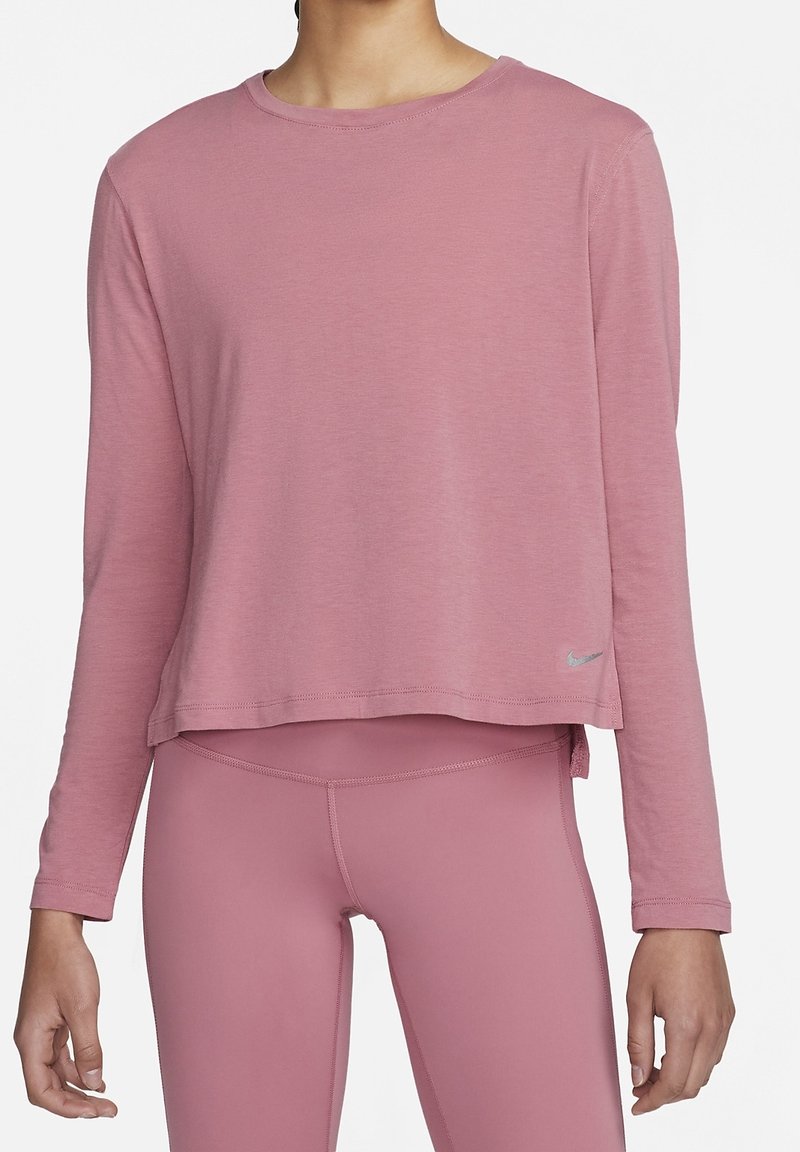 Frau in einem staubigen rosa Langarm-Crop-Top und passenden hochgeschnittenen Leggings, beide aus dehnbarem Sportstoff.