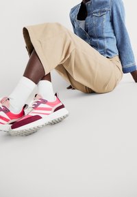 Sportovní tenisky v růžové, bílé a burgundské barvě; texturovaná podrážka; polstrovaný límec; síťovina a semišové materiály.