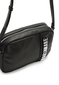 Schwarze Umhängetasche aus synthetischem Leder mit Reißverschluss, rechteckiger Form und einem dekorativen Riemen mit geprägtem Schriftzug. Glatte Oberfläche.