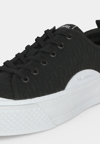 Μαύρο sneaker χαμηλής κορυφής με υφασμάτινη υφή, μαύρα κορδόνια και παχύ λευκό πέλμα με ανάγλυφο το όνομα της μάρκας στο πλάι.
