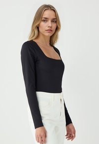 Body nero a maniche lunghe con scollatura quadrata, texture liscia, design aderente; abbinato a pantaloni bianchi a vita alta.