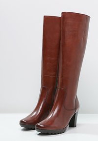 Botas altas hasta la rodilla de cuero marrón con un diseño elegante, acabado texturizado y un tacón grueso y alto. Incluyen una cremallera lateral y costuras prominentes.