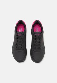 Black athletic sneakers featuring a textured upper, breathable perforations, and pink accents on the tongue and inside lining.
