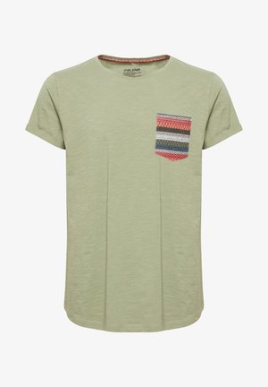Tricou scurt cu mânecă scurtă, de culoare verde deschis, cu guler rotund și un buzunar colorat cu un model zigzag în nuanțe de roșu, albastru și alb.