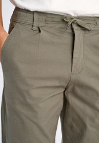 Pantalons vert olive en tissu léger, dotés d'une fermeture à cordon de serrage et de poches latérales. Texture lisse avec un motif de tissage fin et subtil.